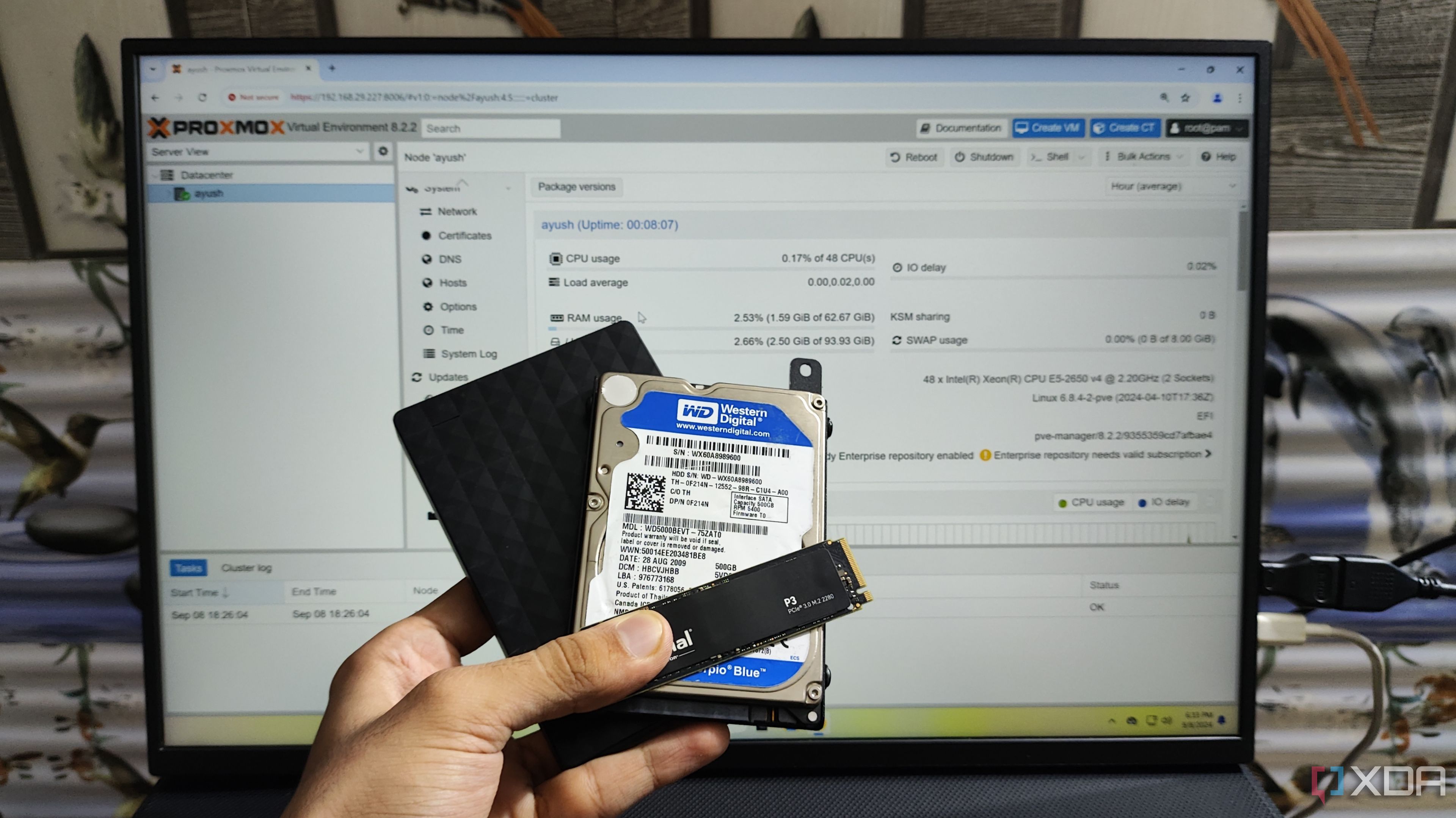 Человек держит SSD, внутренний HDD и внешний HDD перед монитором, на котором отображается пользовательский интерфейс Proxmox.